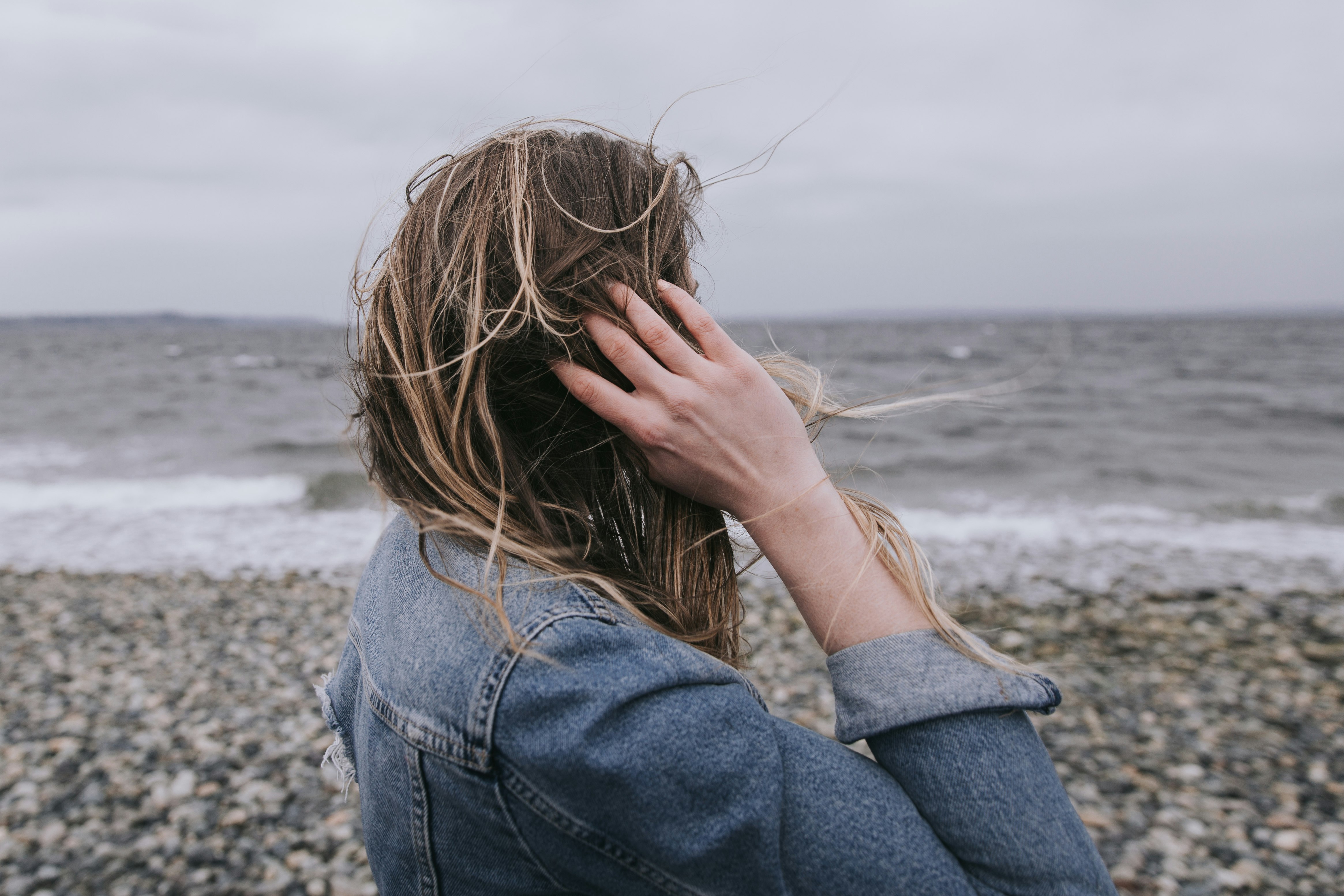 woman in blue denim jacket covering her face with her hands